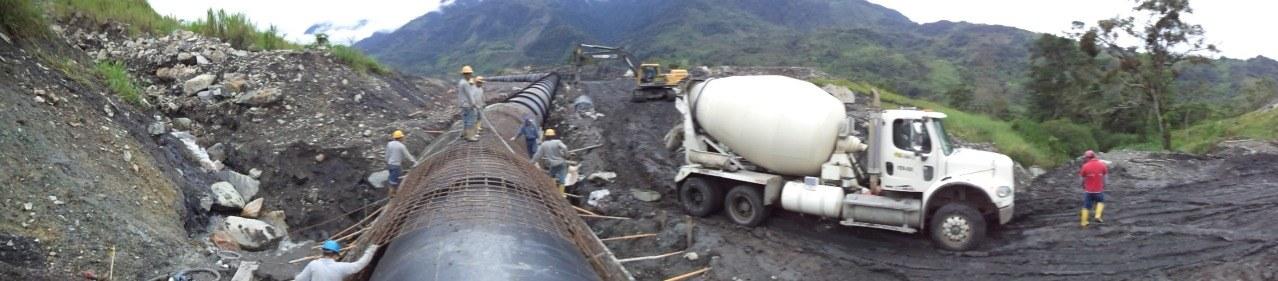 Tubería de conducción en su zanja, con un mixer de hormigón y trabajadores al lado