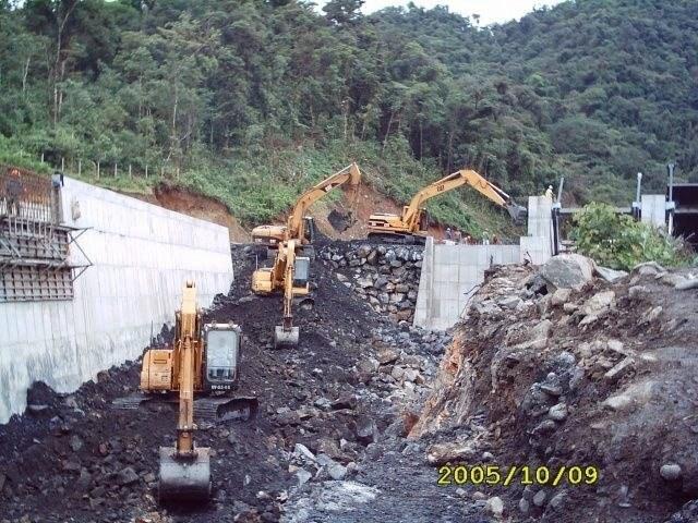 Excavadoras retirando roca junto a un muro de hormigón recién vaciado