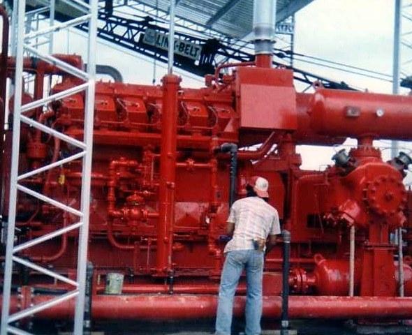 Operario de espaldas junto a un paquete compresor rojo, entre torres de celosía