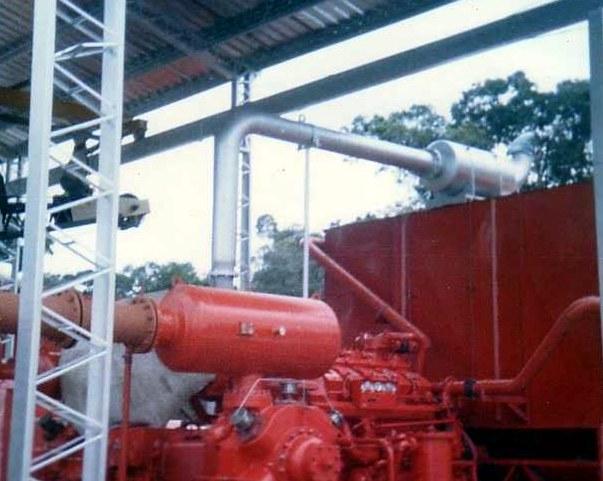 Compresor rojo bajo cubierta metálica, con tubería aérea y torre de celosía