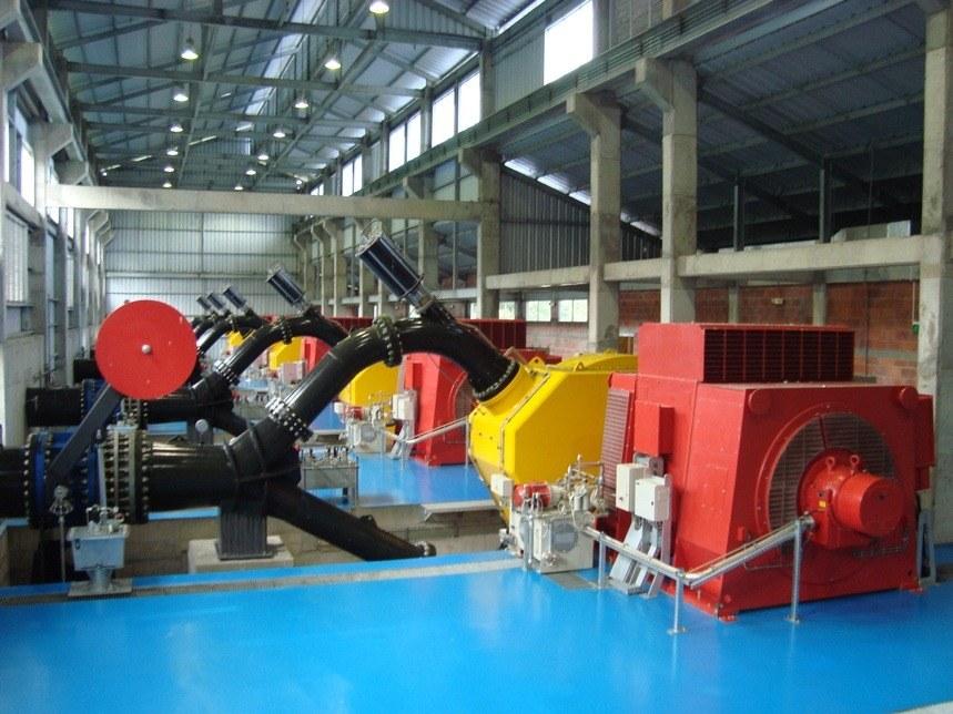 Sala de máquinas con los grupos turbina-generador en fila sobre piso azul
