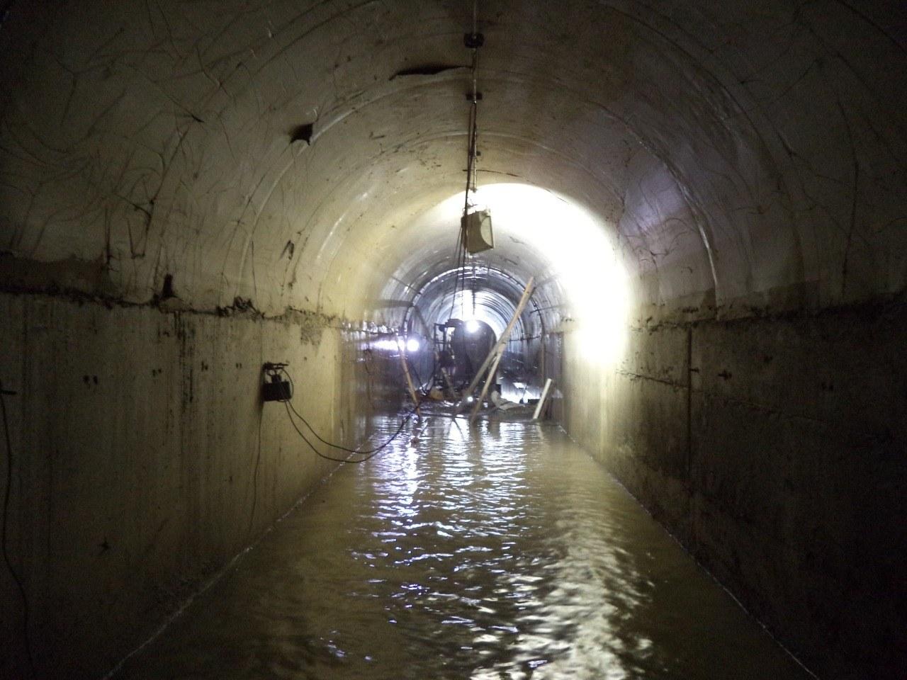 Túnel revestido de hormigón con agua en la solera y luz al fondo